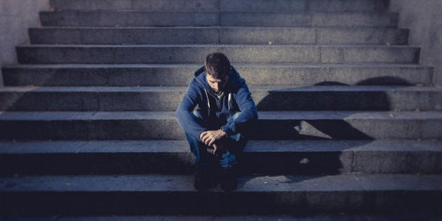 Young desperate man in casual clothes abandoned lost in depression sitting on ground street concrete stairs alone suffering emotional pain, sadness, looking sick in grunge lighting