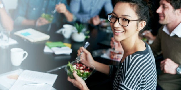 Portrait of a young office worker eating lunch with coworkers at a boardroom table