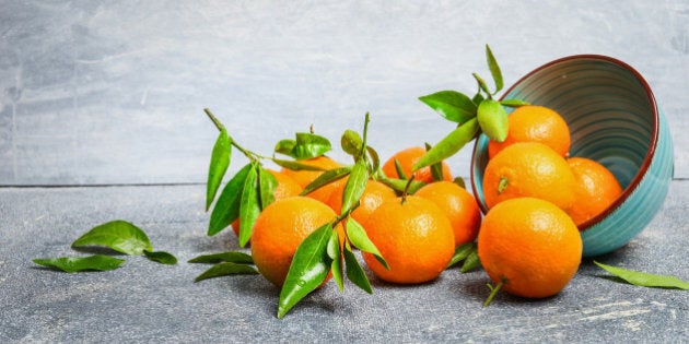 Tangerines with green leaves and bowl on rustic background, side view