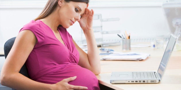 Pregnant woman at work with laptop looking stressed