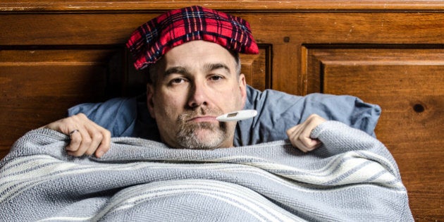 A man sick in bed with a thermometer in his mouth