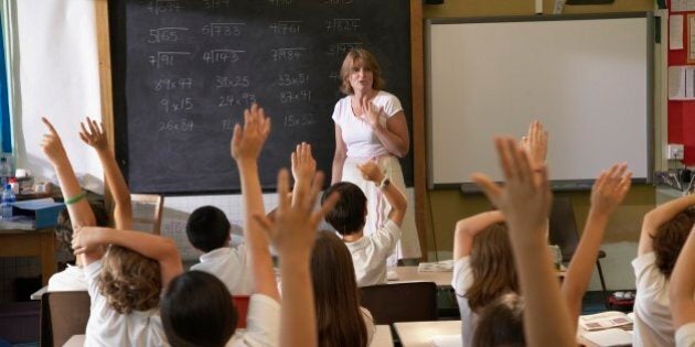 Multi-ethnic children with hands raised in class