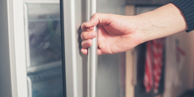 The hand of a young man is opening a freezer door