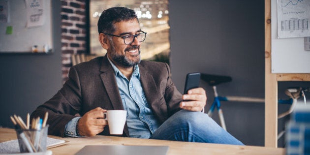 Mature business man working at modern office space. Checking his mobile phone for news or messages. Brick wall and bicycle in background.