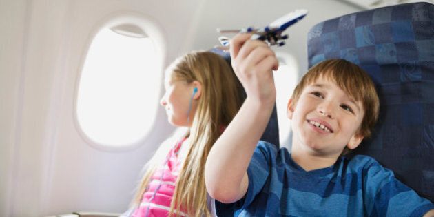 Boy playing with toy plane while sister listens to music in airplane