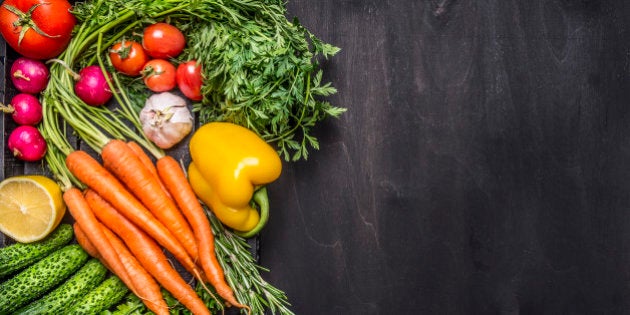 Colorful various organic farm vegetables carrots cherry tomatoes, garlic, cucumber, lemon, pepper, radish, wooden spoon salt pepper colored, oil wooden rustic background top view border, place text