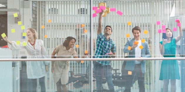 Excited business people with arms raised at window covered in adhesive notes