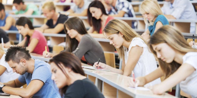 'Group of college students in the university amphitheatre, they are sitting and doing an exam.'