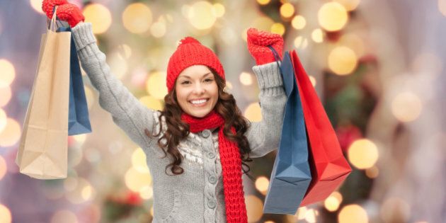 holidays, x-mas, sale and people concept - happy young asian woman in winter clothes with shopping bags over christmas tree lights background