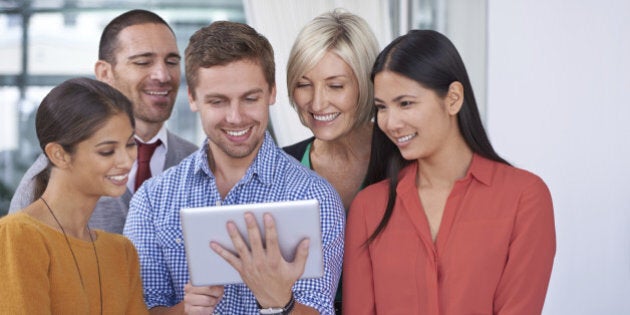 A happy young businessman showing something on his tablet to his coworkers