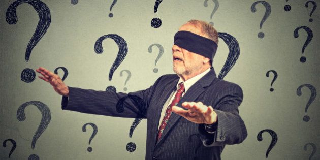 Portrait business man blindfolded stretching his arms out walking through many questions isolated on gray wall background