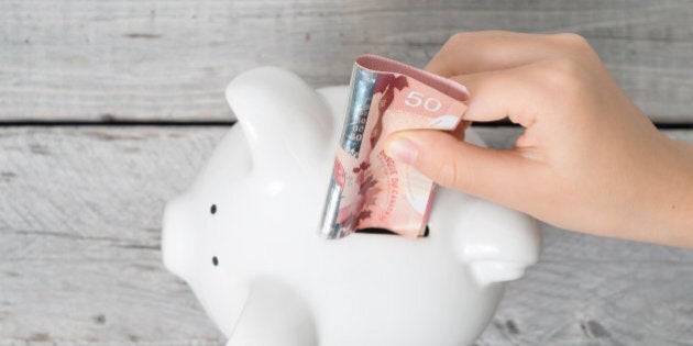 Asian boy hand inserting a fifty dollars bank note into white piggy bank against wooden grey background