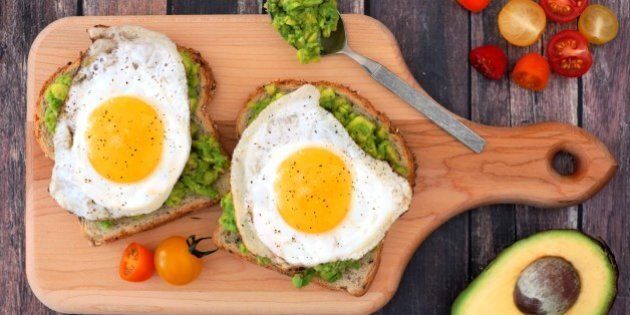 Avocado, egg open sandwiches on whole grain bread with tomatoes on paddle board with rustic wood table