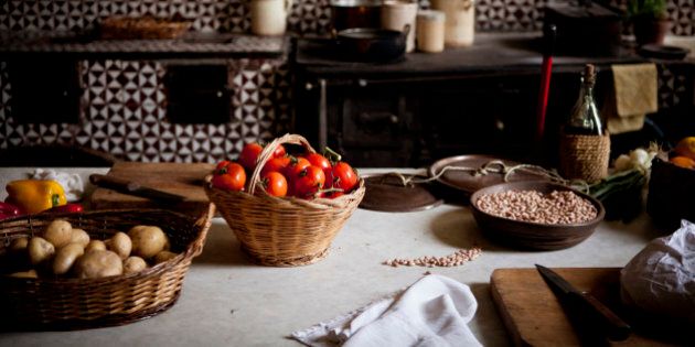 Tomatoes, potatoes, and beans in baskets on a table in a rustic kitchen.