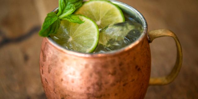 Moscow mule cocktail in a metal copper mug with ice, lemon and mint sprigs on a wooden table