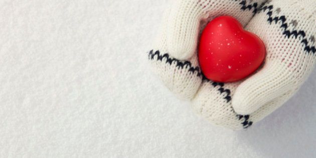 Close up of little girl's hands holding red rubber heart on the snow with copy space