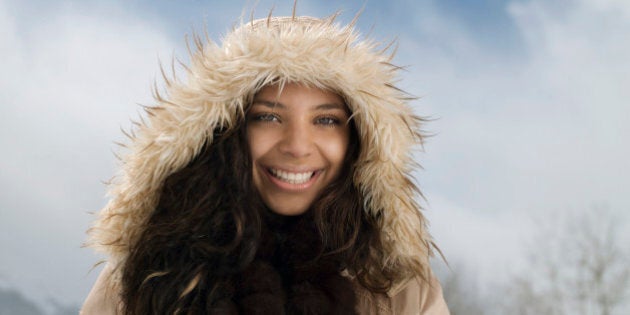 Young woman wearing hooded jacket in snow, smiling, portrait