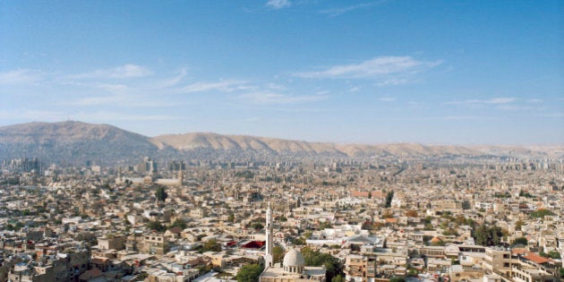 This is a high and wide view of the surrounding neighborhoods of Damascus, Syria. Visible are the rooftops of the homes and businesses of the densely packed city. To the left is the Umayyad Mosque and in the background are the Anti-Lebanon Mountains. Located in southwestern Syria, is not only the country's capital, but a major center for religion, culture, and government.