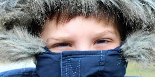 Little boy bundled up in a blue winter coat with fake fur trim around the hood. Winter. Childhood. Humor.