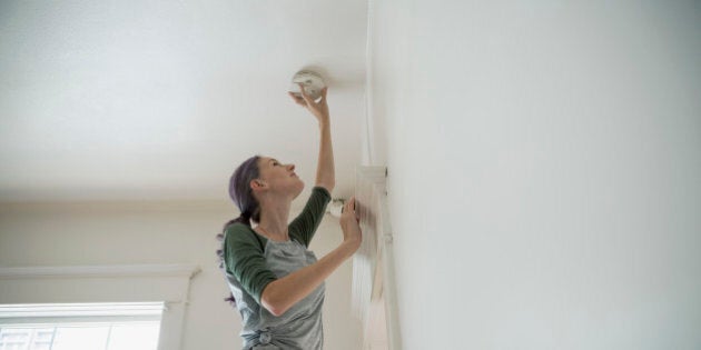 Woman testing smoke detector on ceiling