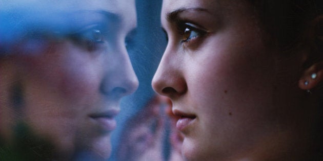 Woman's face close up, staring in mirror with reflection.