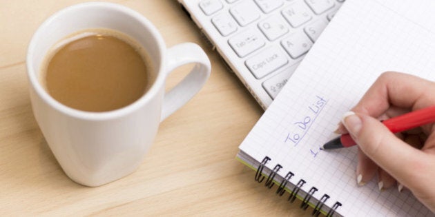 Woman writing a 'to do list' at her desk with a cup of fresh coffee