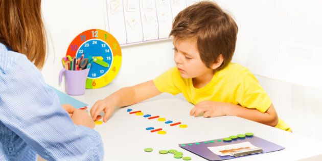 Concentrated boy putting colorful coins in order during developing game with his mother sitting at the table indoors
