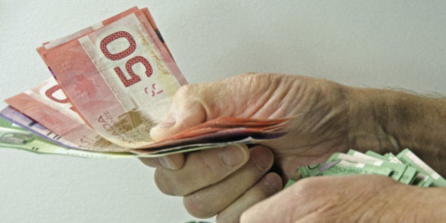 'A man's hands with a large amount of Canadian money handing it out to someone. Money for gifts,bills,mortgage'