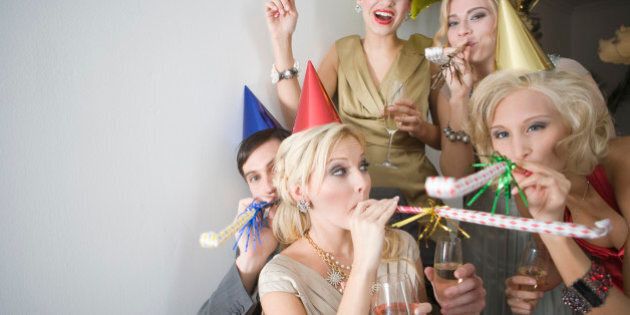 Portrait of young adult friends with party blowers and drinks at Christmas party