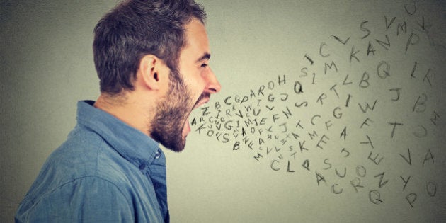 Side profile portrait of young angry man screaming with alphabet letters flying out of wide open mouth isolated on gray wall background