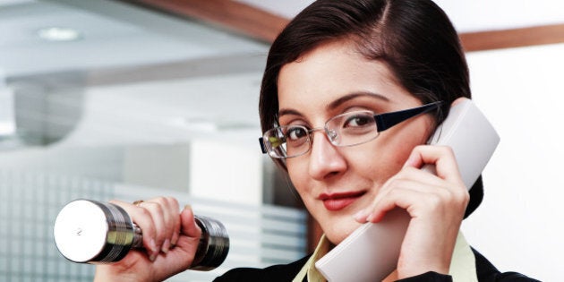 Businesswoman exercising with dumbbells while speaking on telephone