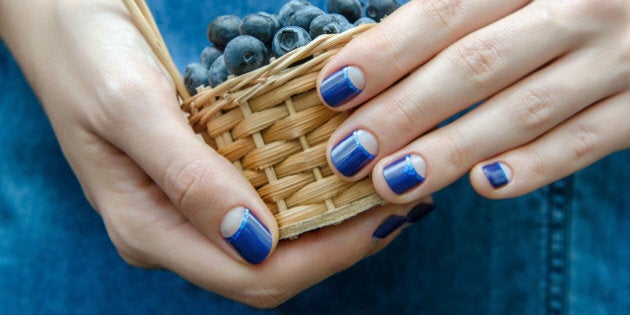 Female hand with blue nail design holding a small basket with berries