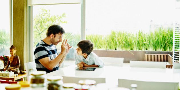 Smiling father and son in discussion while working on digital tablet at dining room table
