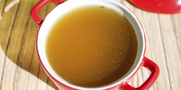 Chicken broth, bouillon, clear soup in a cup next to fresh herbs.