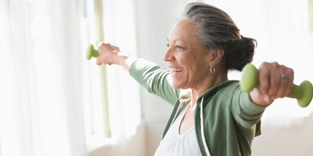 Older Hispanic woman lifting weights in living room