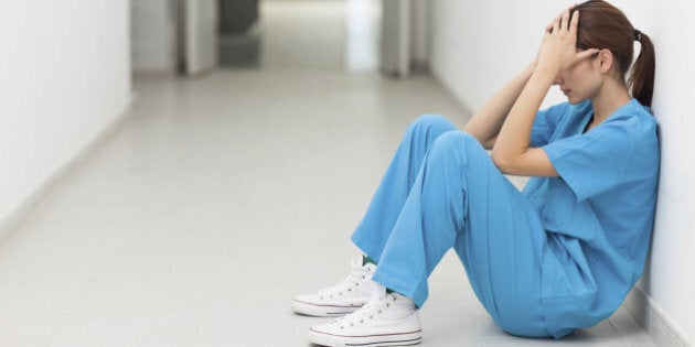 Nurse sitting in a corridor while holding her head in a hospital