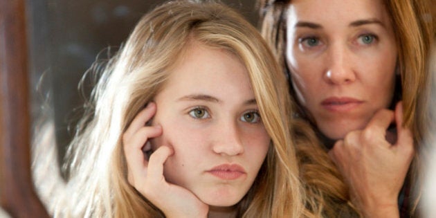 Serious mother and daughter examining themselves in mirror