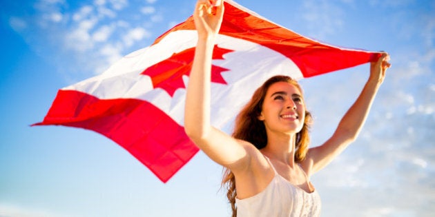 Woman holding canadian flag against blue sky