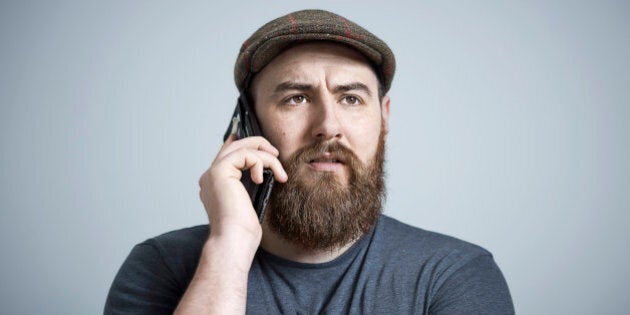 Portrait of bearded male wearing brown cap, making a phone call on smart phone