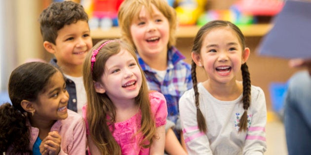 A multi-ethnic group of elementary age children are listening to their teacher read a storybook in class.