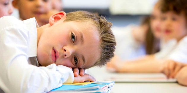 A close up shot of a little boy at school who looks distant and upset.