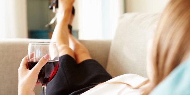 Woman Relaxing On Sofa With Glass Of Wine After Work