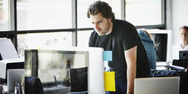 Businessman leaning on desk in office of high tech startup working on computer