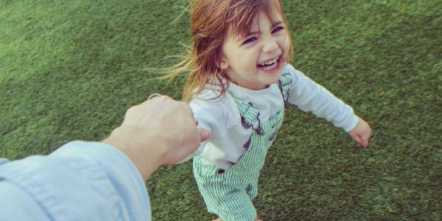 Silly little girl holding a parents hand barefoot in the grass, laughing