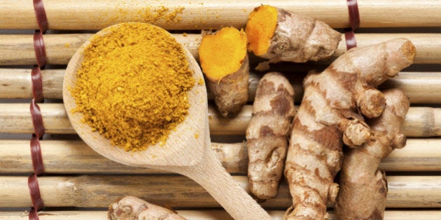 Ground turmeric on wooden spoon and rhizomes on bamboo mat, from above