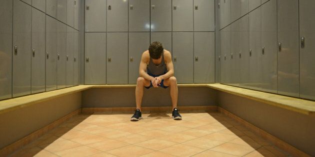 Teenage boy in gym locker room, looking down