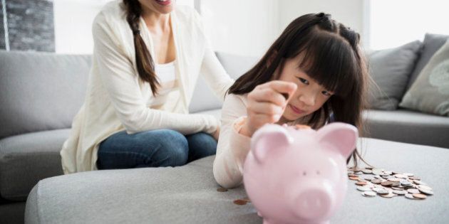 Mother watching daughter deposit coin into piggy bank