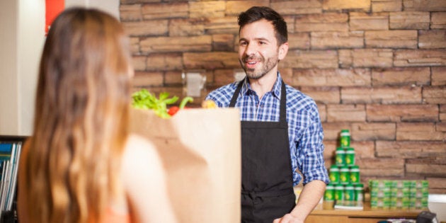 Handsome young male cashier helping a customer at a checkout counter and smiling