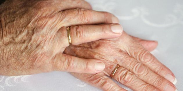 Two hands of an old couple, lying upon each other, with golden wedding rings