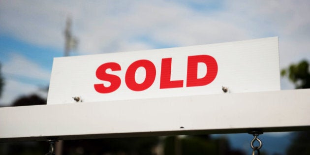 Real estate sold sign against a slightly cloudy blue sky.